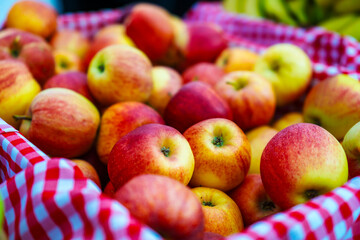 a full basket of freshly harvested red and yellow speckled apples on a checkered cloth concept of farmers market, fresh produce, healthy eating