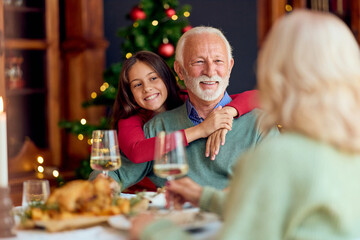 Joyful Family Christmas Dinner With Grandfather And Granddaughter Hugging By the Tree