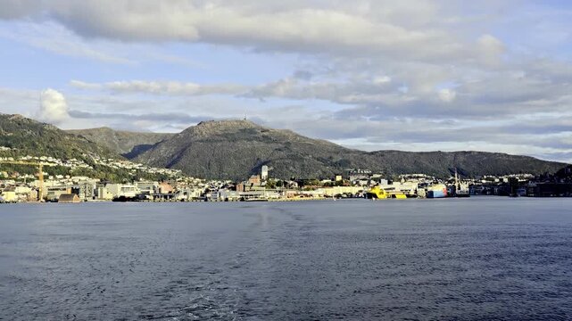 Distant view from aft deck as vessel departs Bergen harbor with skyline and fjord in evening light