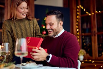 Joyful Couple Sharing Christmas Gift During A Cozy New Year Dinner At Home