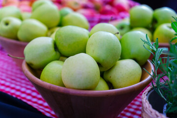 Close-up of fresh green apples displayed in a wooden bowl on a red checkered market table, symbolizing healthy eating and organic produce.
