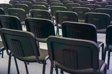 Naklejka premium multiple rows of empty black chairs in a dimly lit conference hall or auditorium concept of corporate meeting, seminar presentation, training event