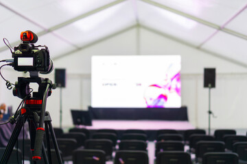 professional video camera on a tripod recording an empty stage and large screen in a white tent concept of event production, live streaming, corporate broadcasting