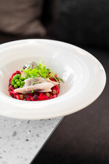 Gourmet beetroot risotto with smoked fish, green peas, microgreens, and leafy greens, artistically plated in a white bowl on a speckled countertop. Top-down view, vibrant colors.