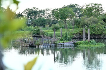 Calm Dongshan River reflecting dense green trees and makeshift floating platform with wooden posts...