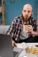 consumption, eating and food delivery service concept. man drinking coffee and eating takeaway food while working online at home