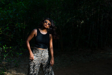 A woman in a black tank top and leopard print pants stands in a forest