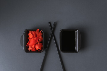 Sushi set served on the black plate next to red ginger with black sticks on the black background. Flat lay