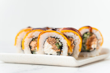 Sushi roll with salmon,  avocado and tuna. Sushi set served on the white plate next to red ginger with wooden sticks on the white background