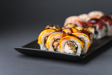 Sushi roll with salmon,  avocado and tuna. Sushi set served on the black plate next to red ginger with black sticks on the black background