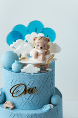 Big two tier birthday cake with blue chocolate frosting decorated with teddy bear flying among the clouds on the plane figurine. Beautiful birthday cake for a little one year old boy. White background