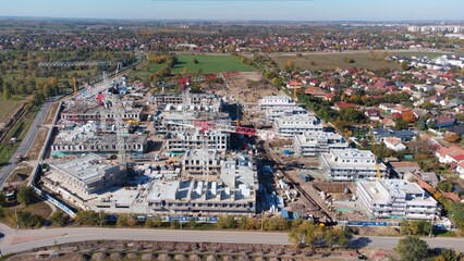 Aerial view of a large modern residential construction site featuring cranes, unfinished buildings, and active development in an urban suburban area. Construction machinery, materials, cranes. 