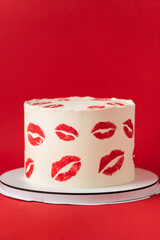 Beautiful birthday white cake decorated with red lips traces pattern. Happy Valentine's cake on the red marble background