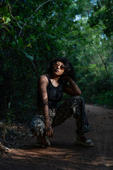 A woman is posing in the woods, wearing a black tank top and leopard print pants