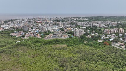 High-resolution aerial photograph showcasing a vibrant coastal city in India, bordered by dense green mangroves and a wide river leading to the sea