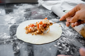 A hand placing meat filling onto a sheet of raw dough while preparing chebureki. Traditional cooking process of making homemade meat pastries, showing close-up details of dough and filling.
