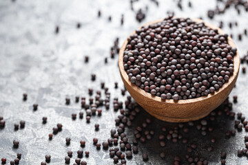 Whole black mustard seeds in a wooden bowl on bright gray surface close-up. Concept of traditional Indian spice and healthy cooking.