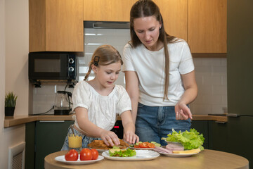 Mother and daughter preparing a nutritious breakfast, spreading ingredients on toast and arranging fresh lettuce, fostering family bonding and shared moments in the kitchen