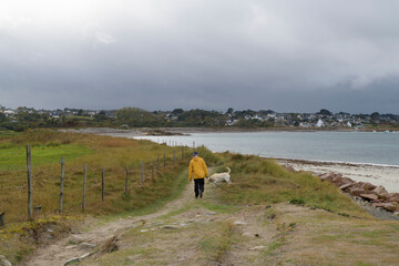 Un homme en ciré jaune qui promène son chien sur la côte en Bretagne