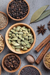 Assorted colorful spices and herbs in wooden bowls on light grey background, top view. Garam masala spices set. Indian spices.