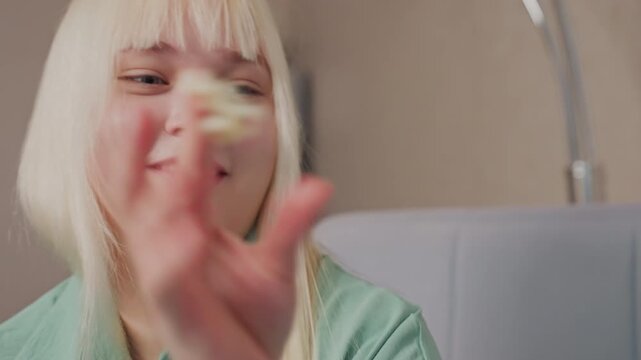 Close up of smiling blonde girl in green shirt tossing popcorn at someone nearby in cheerful playful mood, her joyful expression and relaxed posture reflect lighthearted fun during indoor interaction