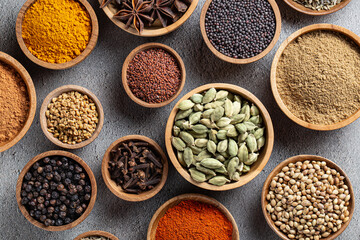 Top view of wooden bowls filled with mixed whole spices and seeds forming circular pattern on table. Concept of flavor variety and traditional cuisine. Indian spices.
