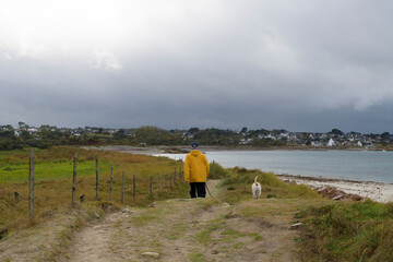 Un homme en ciré jaune qui promène son chien sur la côte en Bretagne