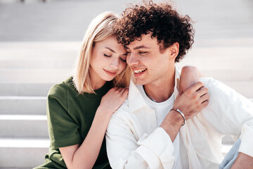 Smiling beautiful woman and her handsome boyfriend. Couple in casual summer clothes. Happy cheerful family. Female and man having fun. They posing in the street in sunny day. sit at stairs