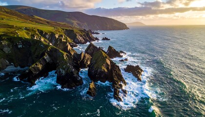 Aerial view of a rugged coastline. Dramatic cliffs plunge into a turbulent ocean, catching the warm light of a setting sun. Green hills