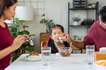 Asian family having dinner, father wiping his young daughter's mouth with a tissue. Parents showing love and care