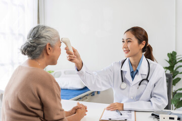Young Asian doctor checking temperature of an elderly woman during a medical consultation in clinic, providing healthcare and care