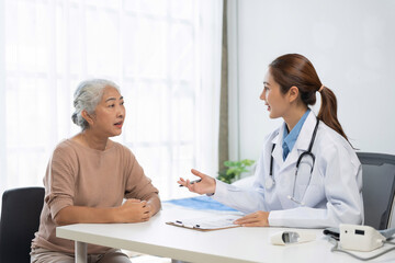 Fototapeta premium Asian doctor talking with an elderly patient during a medical check up, discussing health and providing professional care