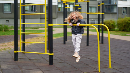 girl playing on playground equipment, smiling and active, enjoying outdoor fun. child in casual clothing on monkey bars in urban park setting offers carefree childhood moments