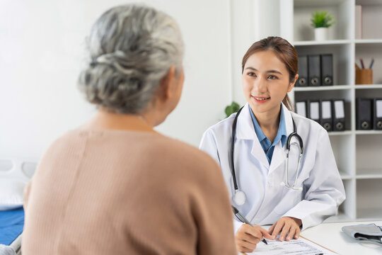 Young doctor talking with elderly woman, providing medical advice and writing notes during a routine clinic examination for senior health