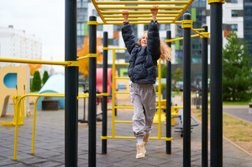 girl on playground climbing bars in urban park, enjoying outdoor activity. dressed warmly,...