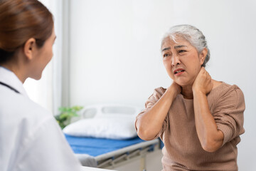 Fototapeta premium Elderly Asian woman describing painful neck to doctor during consultation, showing discomfort and needing medical attention
