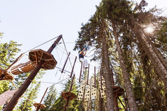Teen girl enjoying zipline ride through tall trees at outdoor adventure park with sun flare.