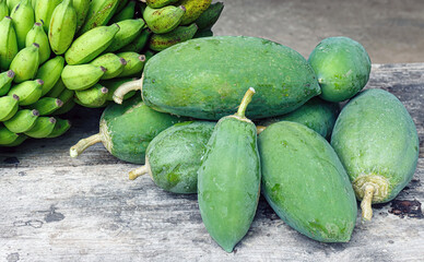 Fresh green bananas and green papaya on wood, shiny with water drops. Tropical produce under natural light.