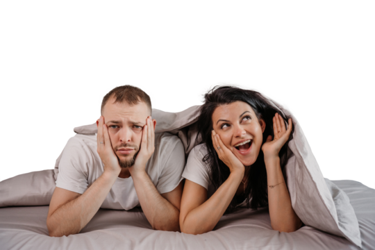 Sad young man laying in bed with cheerful young woman under blanket looks at camera with disappointed face on transparent background . Funny moments, prank. Bored guy wants sleep.