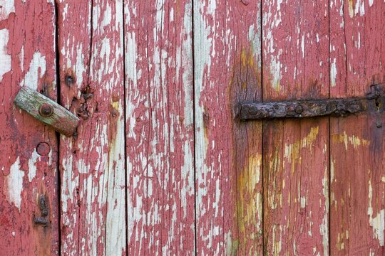 An old wooden door with peeling red paint and a rusty hinge, Mykines, Faroe Islands