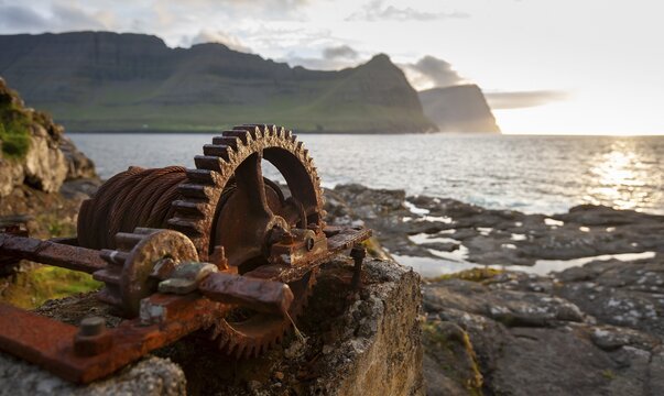 Iron winch with large cogwheel, designed to pull boats ashore, sea with mountains and low sun, Vidareidi, Vidoy Island, Vi&eth;arei&eth;i, Vi&eth;oy Island, Faroe Islands, Denmark