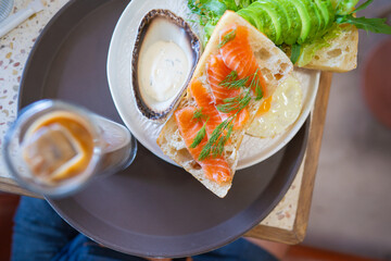 Top view of smoked salmon sandwich with fried egg, avocado, and dill on ciabatta bread, served with sauce