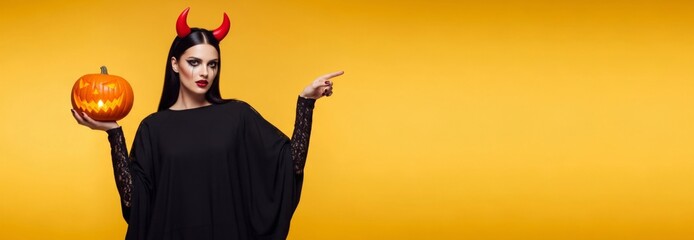 Caucasian woman holding a jack-o-lantern and pointing, on a yellow background, dressed in a devil costume for a Halloween celebration. Banner template for holiday sale with copy space.