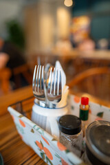 Closeup of forks and condiment bottles in table basket, blurred cafe interior