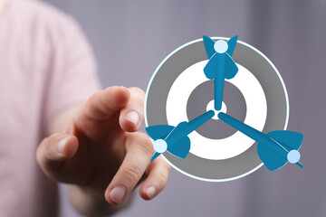 Image of a person's hand pointing at a dartboard with three darts. Concept of achieving goals, success, strategy, and business.