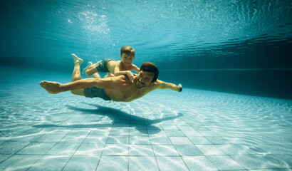 Smiling father and son having fun underwater in swimming pool