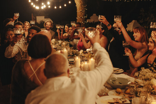 Lively celebration as wedding guests toast together during an outdoor evening reception
