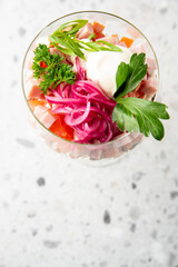 Gourmet fish tartare served in a stemmed glass with creamy sauce, pickled onions, parsley garnish. Elegant fine dining presentation on terrazzo surface.