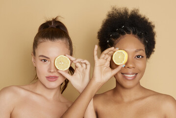 Colorful citrus circles near the face of cheerful multiracial women smiling and holding fresh citrus fruits near eyes while representing vitamin C benefits.
