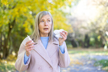Senior woman suffering from autumn allergy holding nasal spray